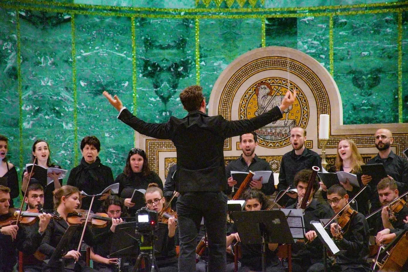Alon Ben Dor conducting orchestra and choir beneath a mosaic apse